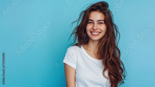 Pretty young smiling woman with dark hair on a blue background with copy space. Cute girl in a simple white T-shirt. photo