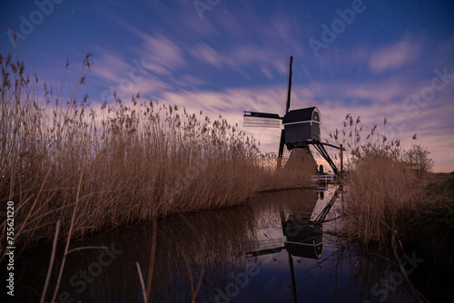 An old Dutch windmill among the reeds at the edge of the river. Broekmolen in a story frame made during the night reflecting in the water under the starry sky