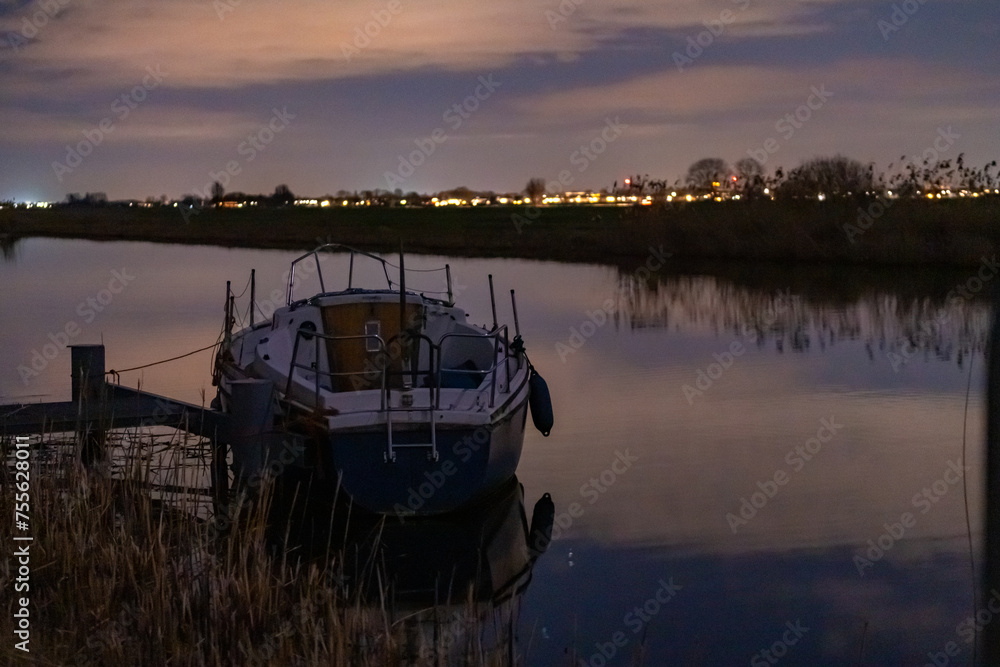 Fototapeta premium A boat anchored among the reeds at the edge of the river. Night landscape in a rural environment with a starry sky somewhere in the Netherlands