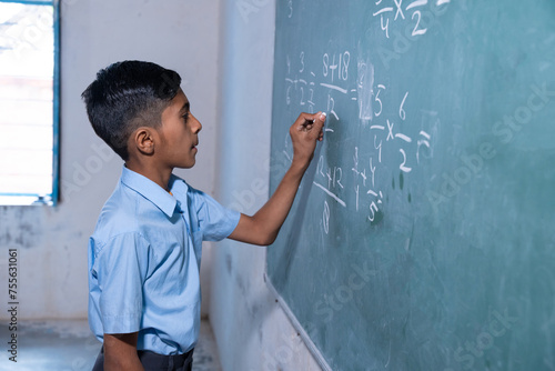 Happy Indian rural school boy write on chalkboard or blackboard in classroom, Education concept. photo