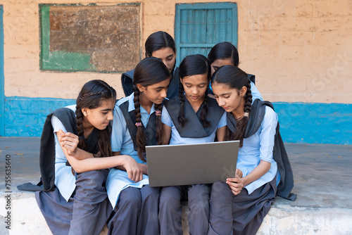Group of rural school girls in uniform sitting in school corridor working on laptop - concept of digital education
