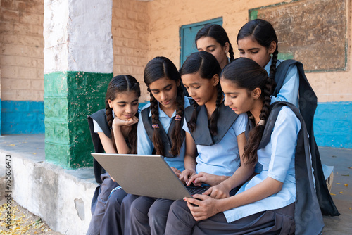 Group of rural school girls in uniform sitting in school corridor working on laptop - concept of digital educationindia