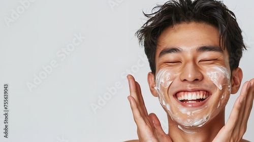 Portrait of a Asian man his cheeks covered in cream, smiles while covering his eyes during a skincare routine against clean background with space for text, Generative AI. photo