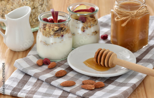 Crunchy granola with yogurt, apple, nuts and honey in glass jars on wooden table. Healthy breakfast concept.