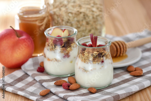 Crunchy granola with yogurt, apple, nuts and honey in glass jars on wooden table. Healthy breakfast concept.