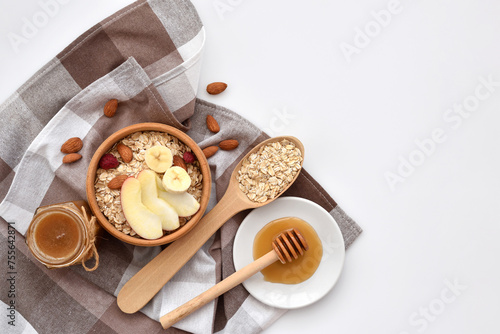 Oatmeal in a wooden bowl with almonds and pieces of apple ready to cook, honey, scattered oat flakes and spoon on white background. View from above. Place for text