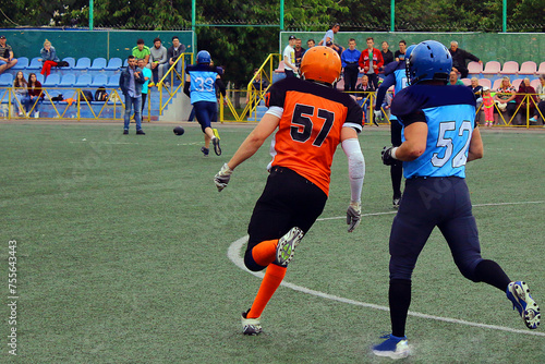 American football players in blue and black uniforms with number 52 runs after an opponent in orange and black uniforms with number 57 