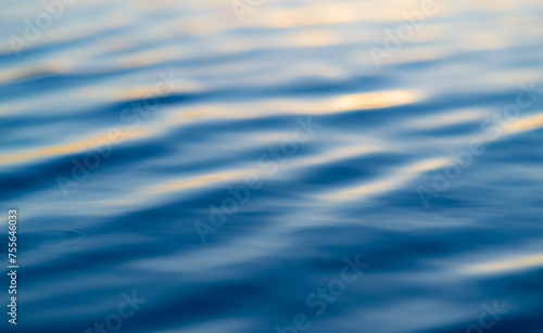 Blurred liquid background with bright blue and orange colors. Wavy water surface with reflection of blue evening sky at sunset. Blue hour twilight at a big lake in Sauerland, Germany. 