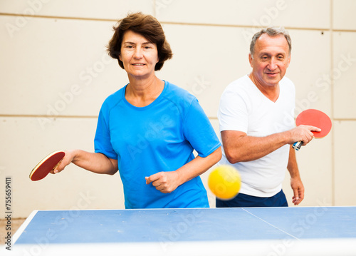 Happy mature man and woman playing table tennis