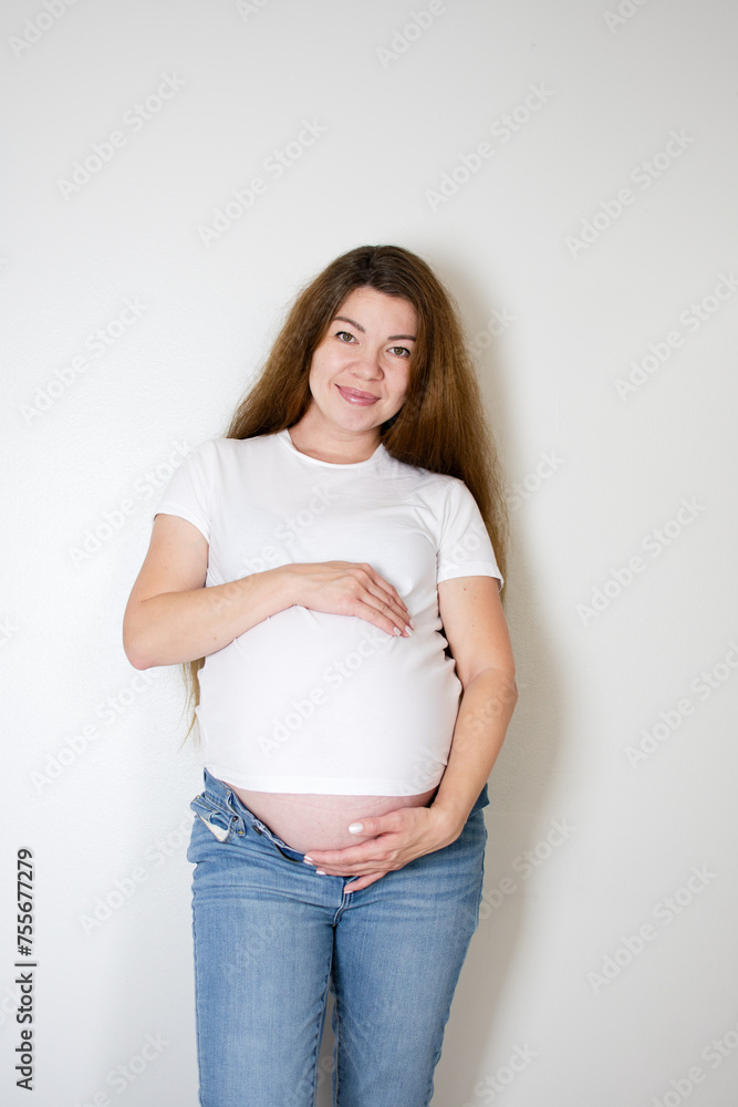 36-week pregnant Caucasian woman in a white t-shirt and jeans holding her belly. Expecting mother 36-week pregnant Caucasian woman in a white t-shirt and jeans holding her belly. Expecting mother