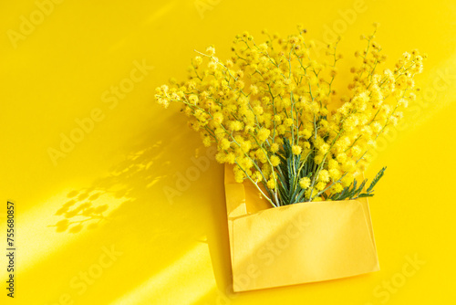 Bright Mimosa flowers in a yellow envelope on yellow background photo