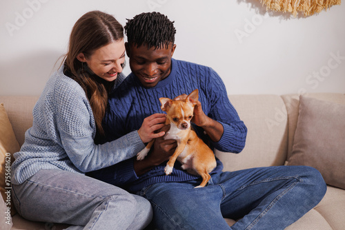 Smiling interracial couple petting chihuahua dog on couch at home