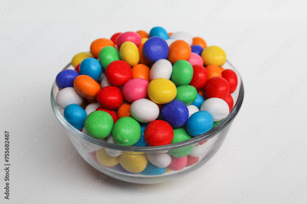 Biscuit balls coated by colorful chocolate. On transparent glass bowl. Isolated on white background
