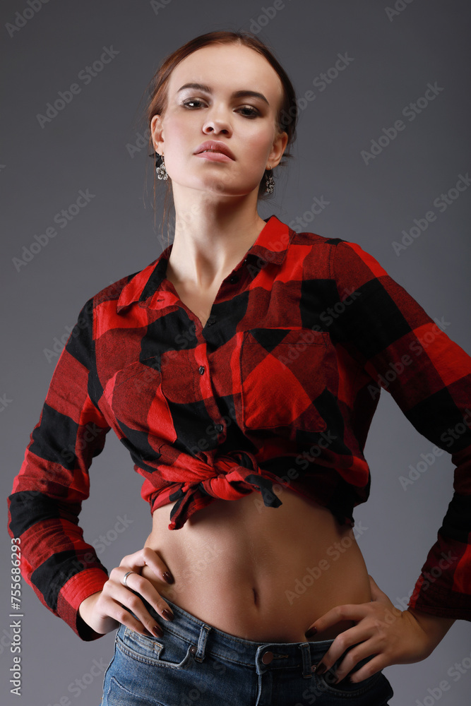 Young beautiful woman in red checkered shirt poses in grey studio - obrazy, fototapety, plakaty 