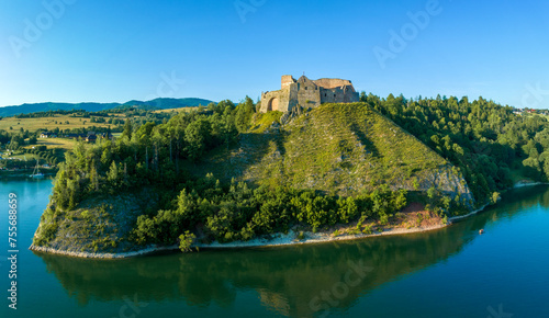 Ruins of medieval castle in Czorsztyn, Poland. Aerial panorama in summer in sunset light. Artificial Czorsztyn lake on Dunajec River. Water reflection and a small tourist boat