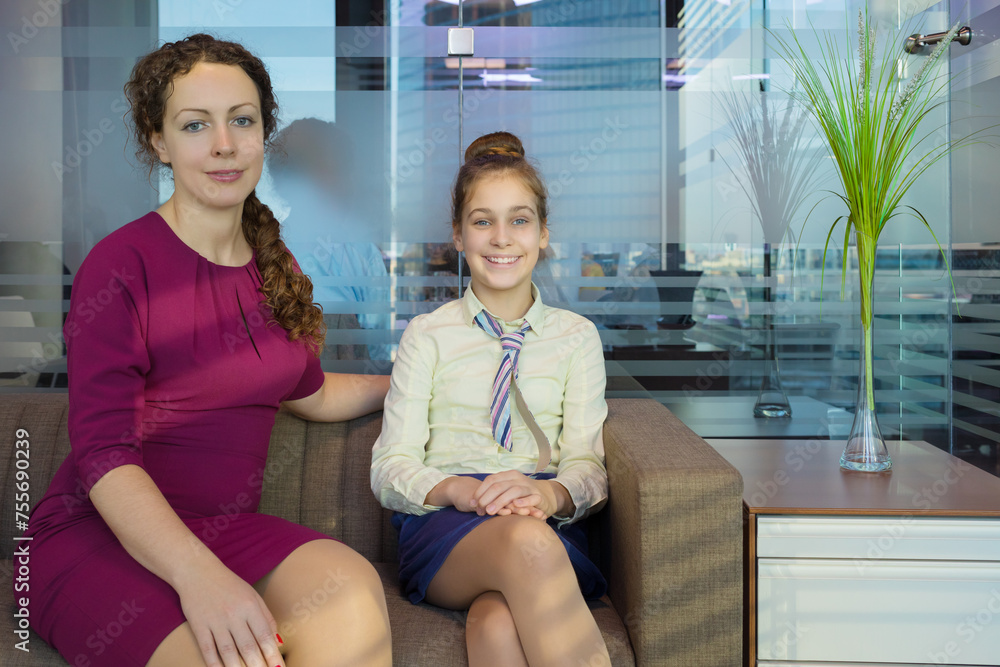 Fototapeta premium Pretty girl in tie and woman smile on sofa in modern office with glass walls