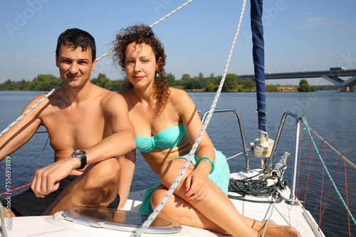 Happy couple sails on yacht on river with bridge at sunny summer day