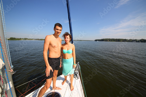 Man and woman stand together on snout of yacht on river at summer day