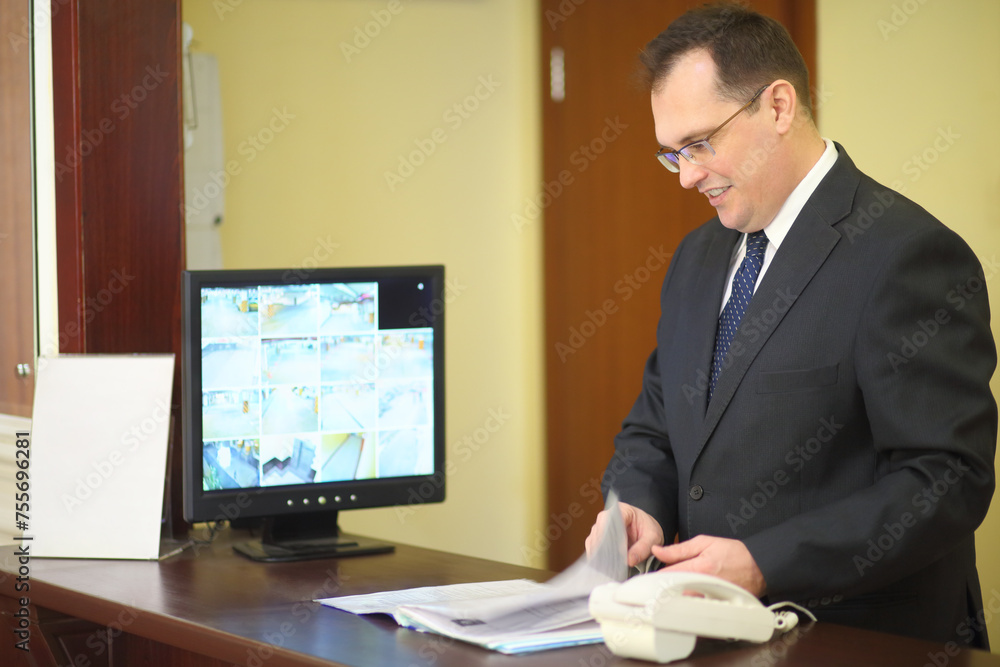 Concierge behind the counter at his workplace leafing through a magazine in a luxury apartment building