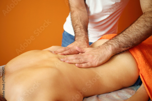 Masseur in white massages back of young woman in room, noface
