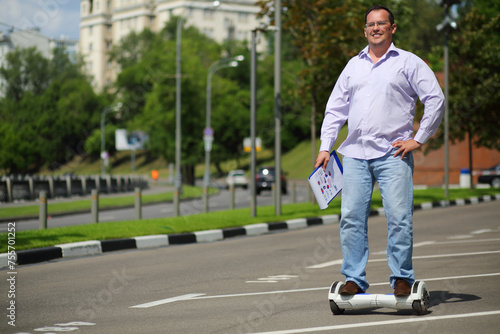Happy man with documents rides GyroScooter on street at sunny summer day photo