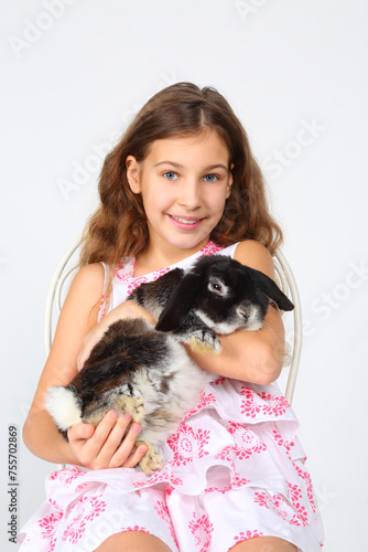 Принти на полотні Happy smiling girl in dress holds funny rabbit and sits on chair in white studio