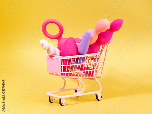 anal plugs and dildo sex toys in shopping basket over yellow backdrop