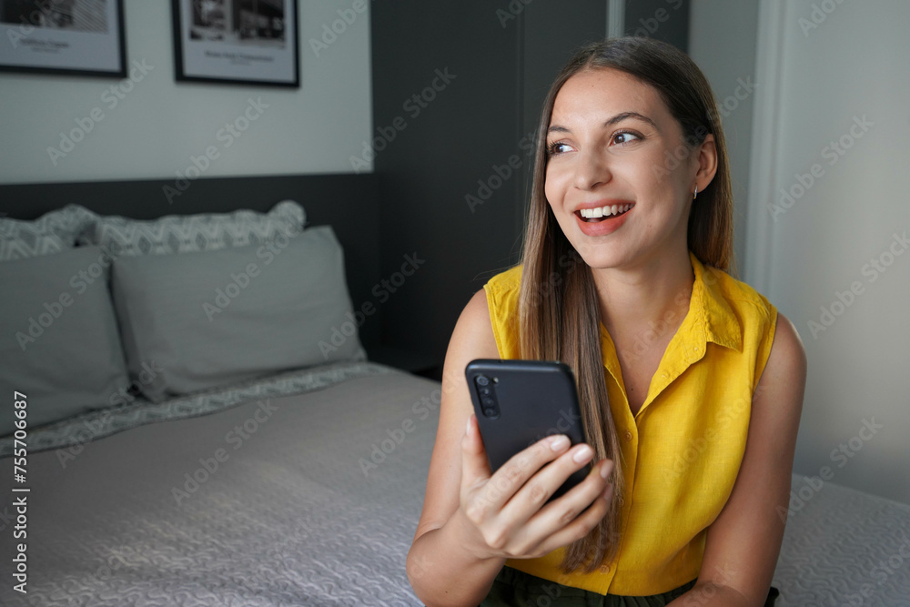 Positive young woman using smartphone at home. Internet connection technology, looking away in deep thoughts, thinking over message. Positive young woman using smartphone at home. Internet connection technology, looking away in deep thoughts, thinking over message.