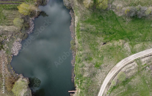 A dirt road near a village pond in the middle of a green meadow. Aerial view.