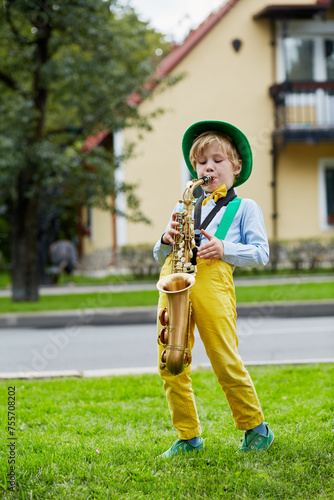 Little boy in dancing suit plays saxophone on grassy lawn against two-storied house photo