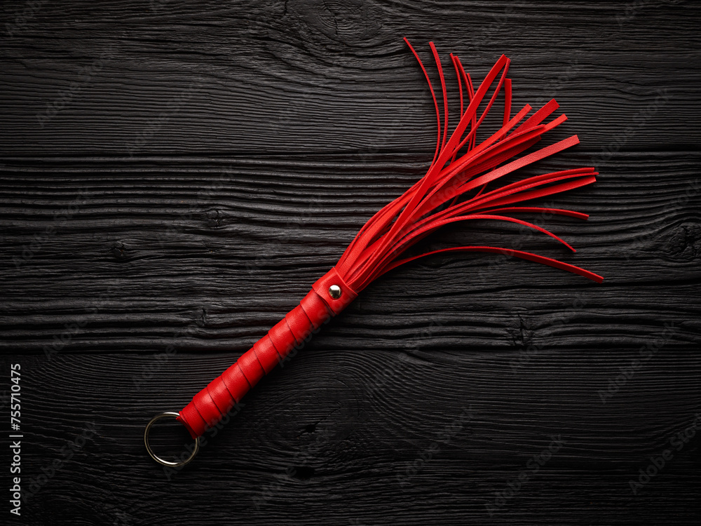 Red whip for adult role play games over black wooden background - obrazy, fototapety, plakaty 