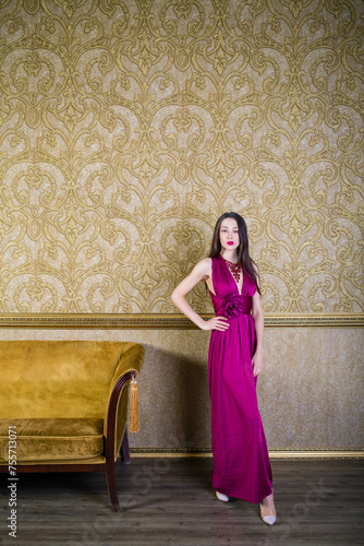 Slim girl in long dress stands near wall in room