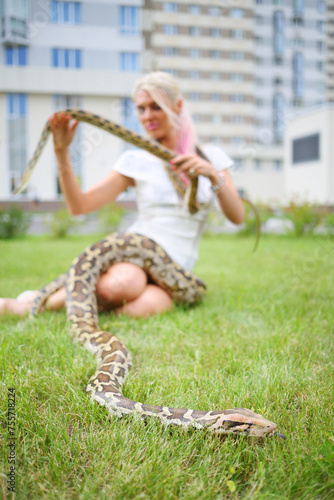 Pretty woman with two snakes on green lawn near building, focus on snake