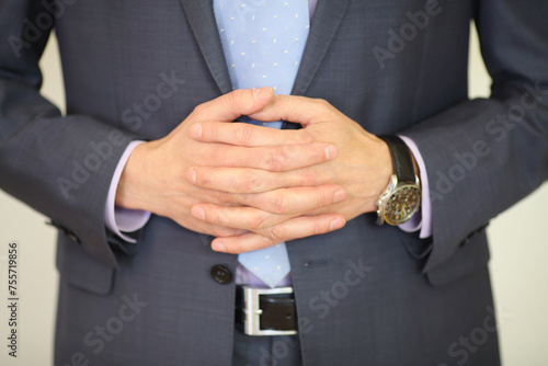 Hands of man in suit poses with folded hands and wristwatch in studio, noface