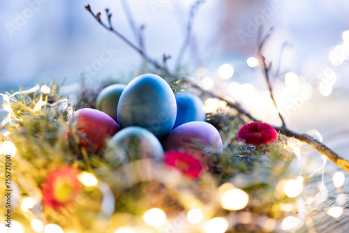 Colorful easter eggs in a herb nest with spring flowers on weathered rustic wooden table. Background with bokeh lights and short depth of field. 