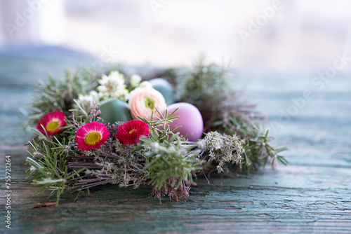 Colorful easter eggs in a herb nest with spring flowers on weathered rustic wooden table. Background with short depth of field and space for text.