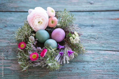 Colorful easter eggs in a herb nest with spring flowers on weathered rustic wooden table. Top view with space for text.