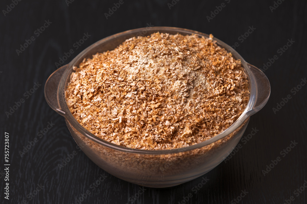 Wheat graham flour in glass bowl on black wooden background Wheat graham flour in glass bowl on black wooden background