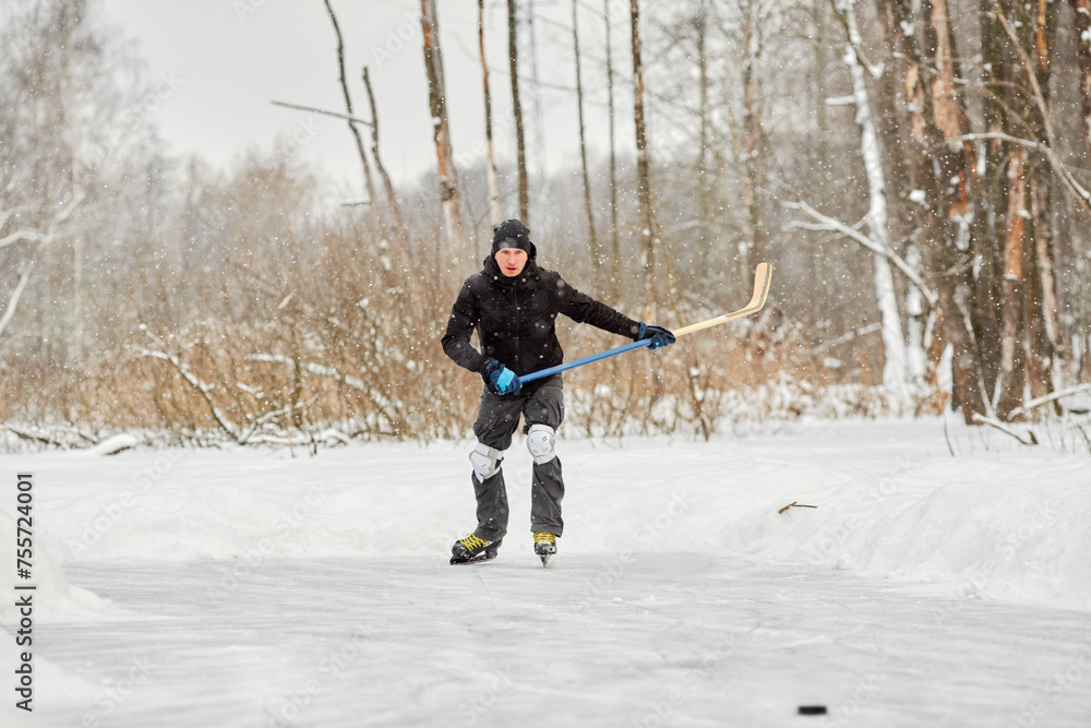 Young man plays hockey at outdoor skating rink in park