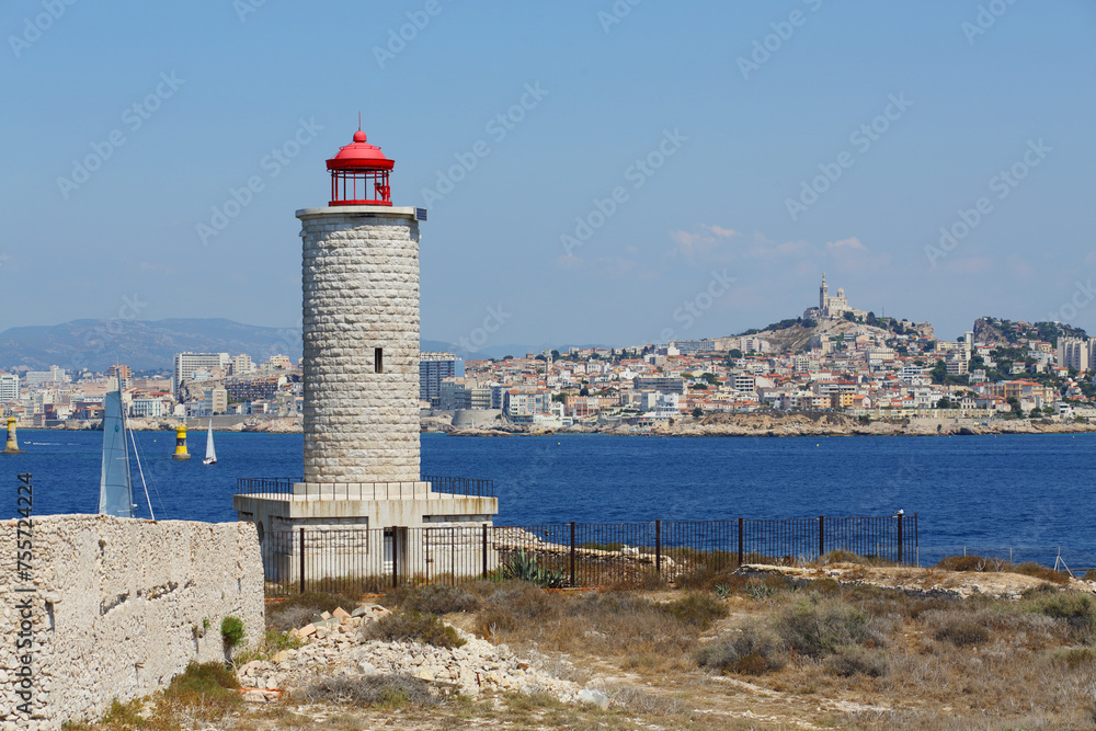 Lighthouse on IF island and yachts sail near coastal city with Notre-Dame De La Garde cathedral in Marseille, France