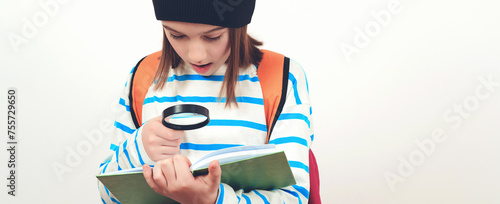 Boy looking through magnifying glass to the book. Schoolboy holding the magnifying glass. Children's interest. Portrait of student boy with magnifier.