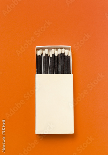 Black matches in a box on a orange background.