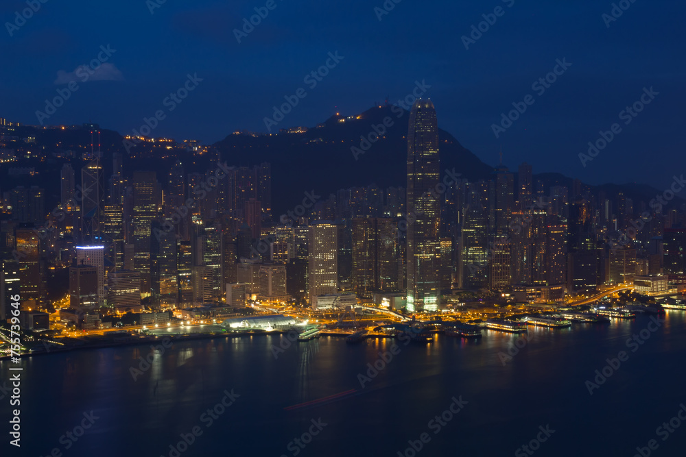 Skyscrapers with bright illumination, shore front and mountains in Hong Kong, China at dark night, view from New World Center