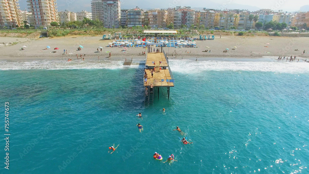 Many people swim in sea near pier on city beach at summer sunny day. Aerial view videoframe