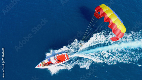 People fly on parachute attached to motorboat with group of tourists at summer sunny day. Aerial view videoframe photo