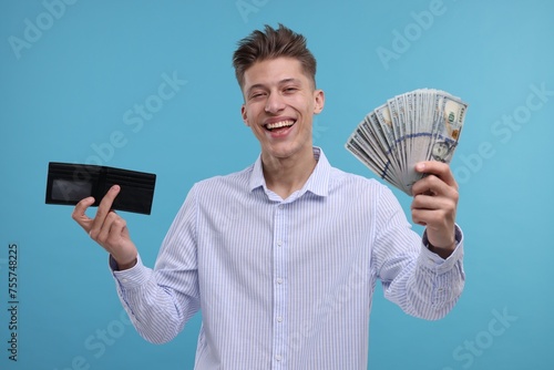 Happy man with wallet and dollar banknotes on light blue background