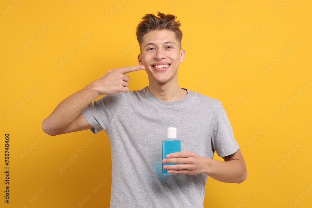 Young man with mouthwash pointing at his healthy teeth on yellow background Young man with mouthwash pointing at his healthy teeth on yellow background