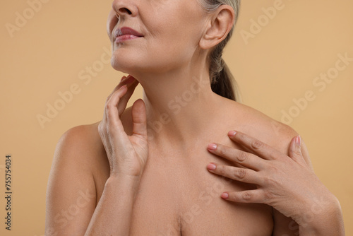 Mature woman touching her neck on beige background, closeup