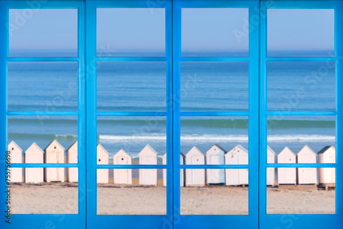 Blue window with a view on a beach with vintage white cabins