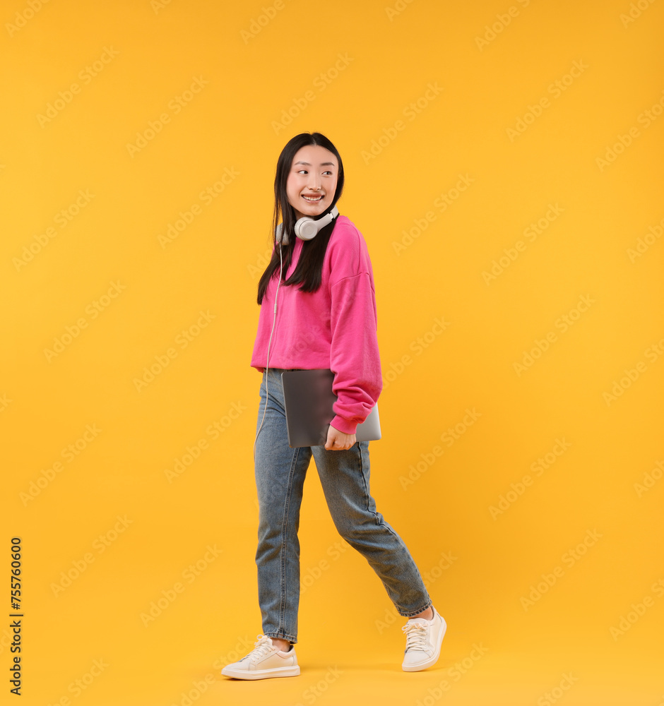 Portrait of smiling woman with headphones and laptop on orange background Portrait of smiling woman with headphones and laptop on orange background
